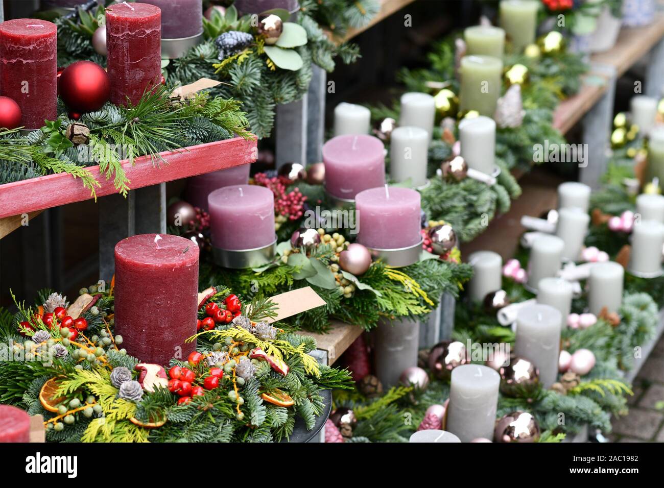 Tradizionale ghirlande con unico grande rosso scuro, rosa e candele bianche e stagionali per le decorazioni di Natale sul ripiano in legno per la vendita di fronte fl Foto Stock