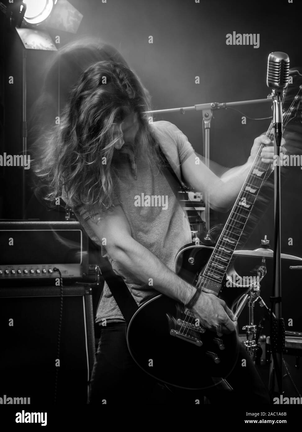 Foto di un giovane uomo di suonare una chitarra elettrica sul palco e lanciare i suoi lunghi capelli intorno a. Movimento sfocate con doppia esposizione. Foto Stock