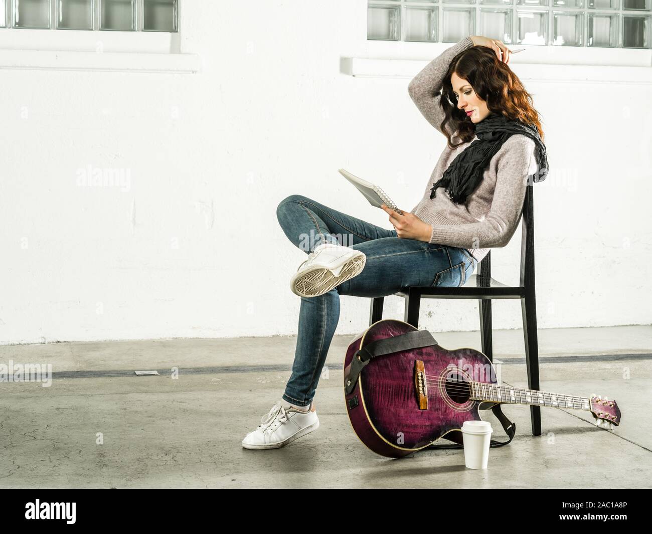 Bella redhead seduto su una sedia a scrivere canzoni con la chitarra acustica accanto a lei. Foto Stock
