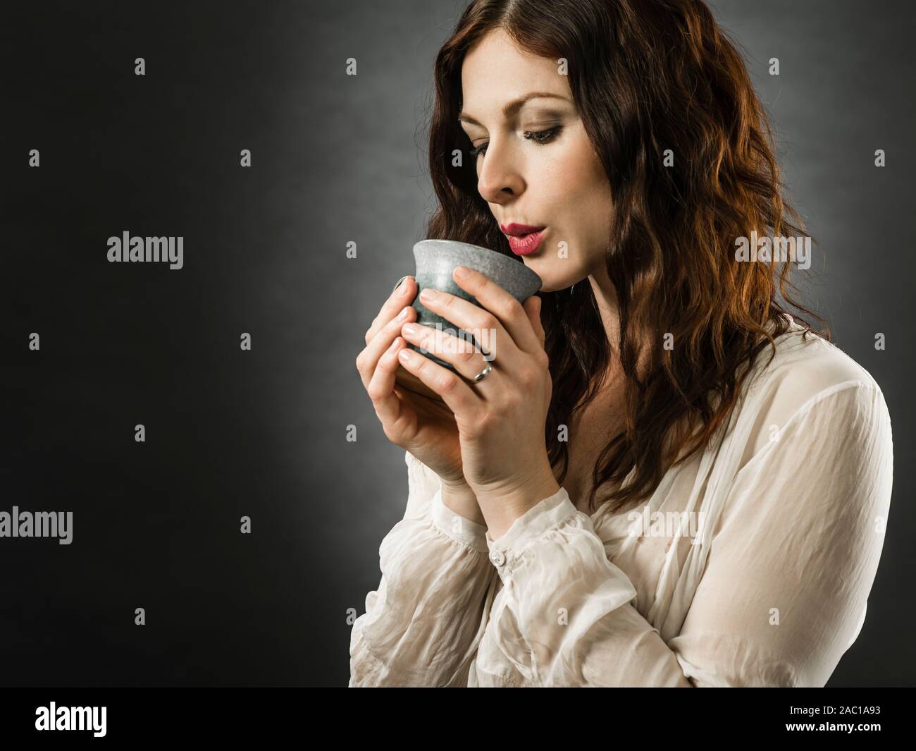 Bella felice redhead donna che soffia sul suo caffè caldo. Foto Stock