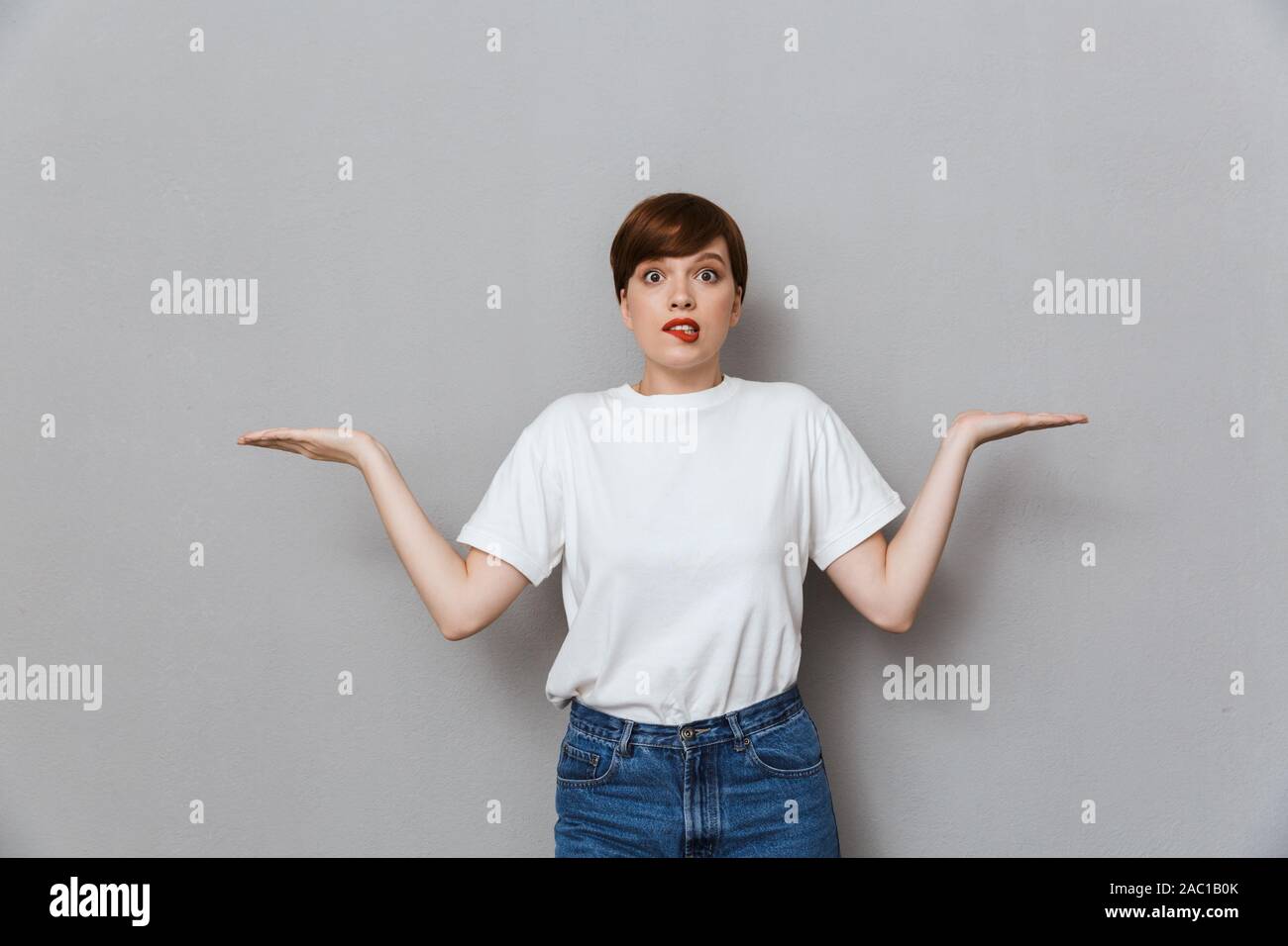 Immagine di perplesso giovane donna scrollare e alzare le mani isolate su uno sfondo grigio Foto Stock