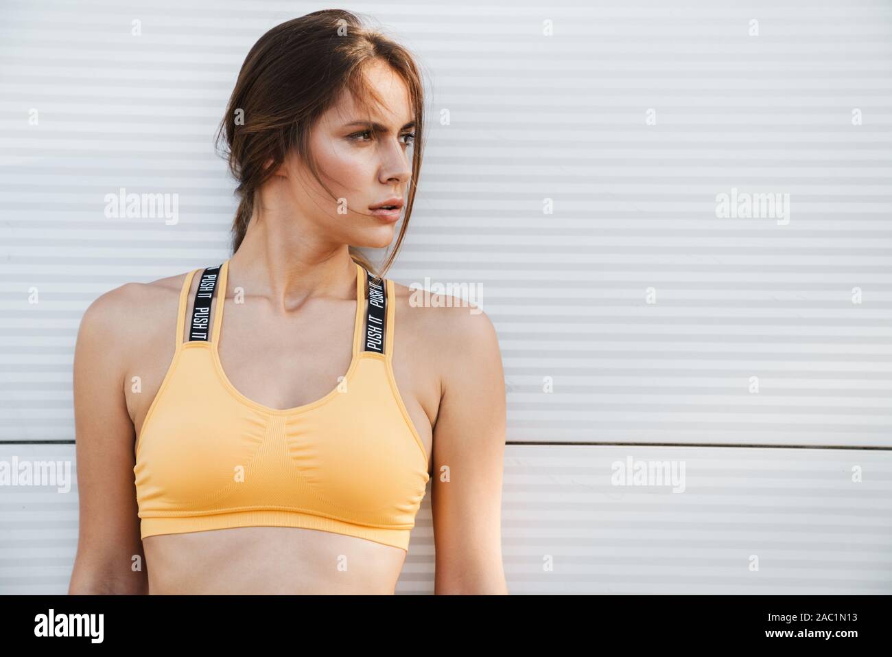 Primo piano immagine di donna attraente in sportswear in piedi su muro bianco all'aperto sul giorno di estate Foto Stock