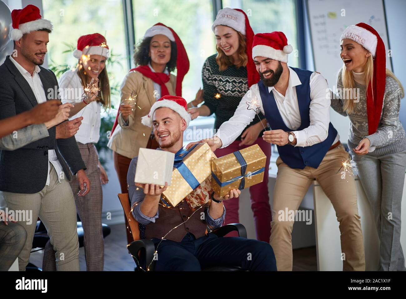 Festa di Natale al lavoro. Felici i giovani imprenditori a santa con cappello di Natale presente Foto Stock