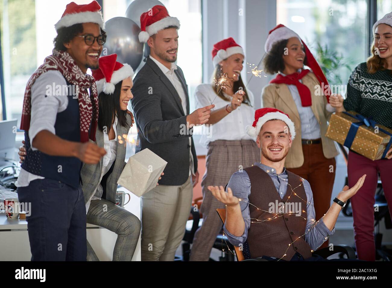 Xmas Party al lavoro. Sorridente giovane gente di affari in santa con cappello di Natale presente Foto Stock