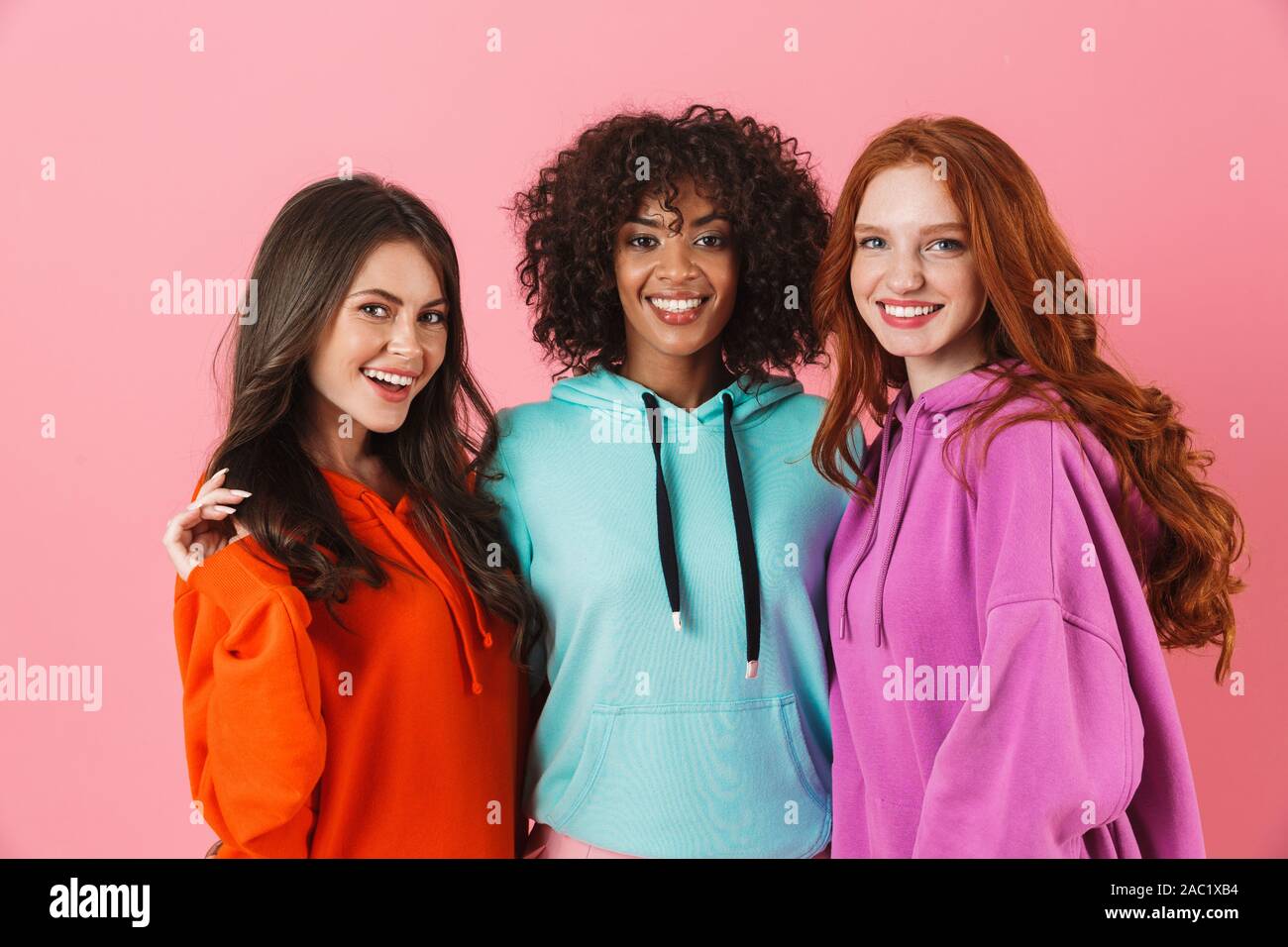 Tre Allegri ragazze multietnica in piedi isolato su sfondo rosa, avvolgente Foto Stock