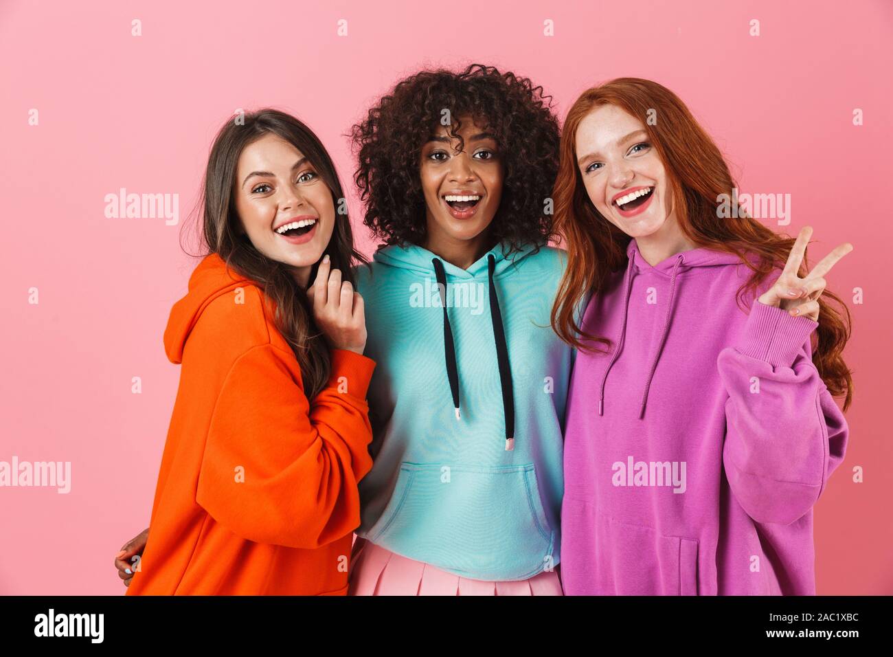 Tre Allegri ragazze multietnica in piedi isolato su sfondo rosa, avvolgente Foto Stock