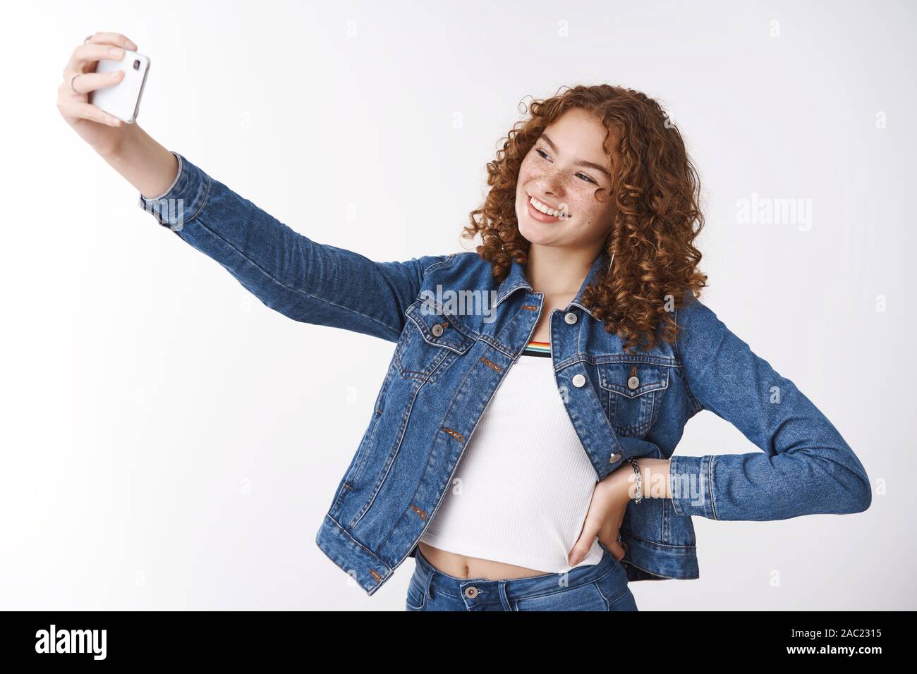 Gentile in uscita giovani attraenti redhead curly ragazza brufoli e  lentiggini tenere la mano alla cintura fiducioso estendere il braccio  tenendo selfie nuova fotocamera dello smartphone Foto stock - Alamy
