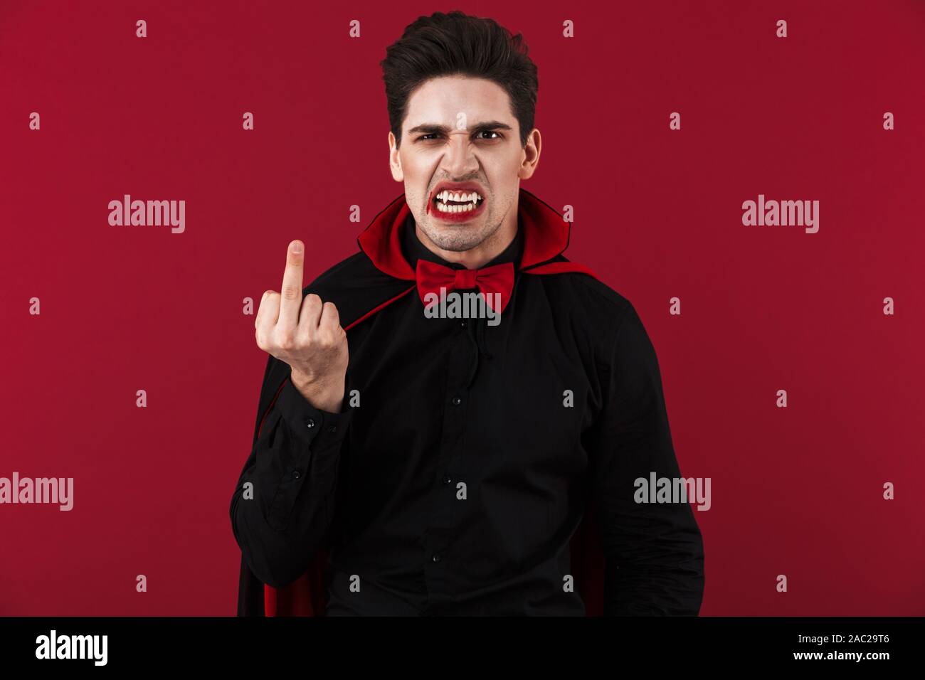 Immagine del vampiro spaventoso uomo con sangue e zanne in black costume di  halloween che mostra il dito medio isolato sulla parete rossa Foto stock -  Alamy