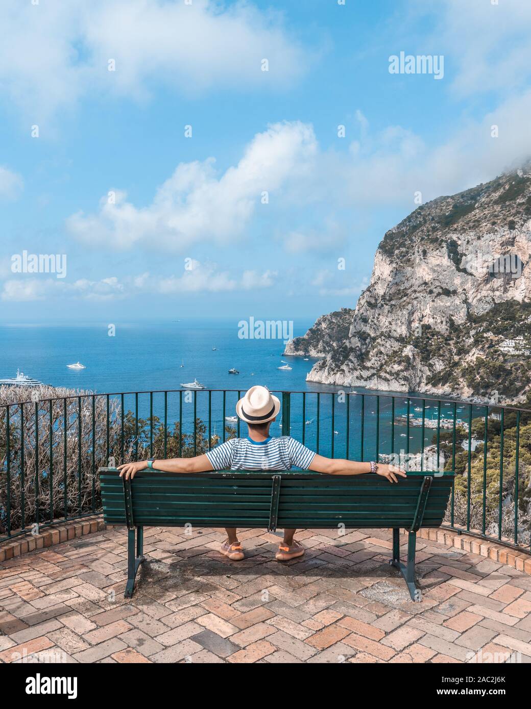 Uomo che indossa hat sedersi su una panchina guardando oltre il mare Tirreno in Giardini di Augusto a Capri Foto Stock