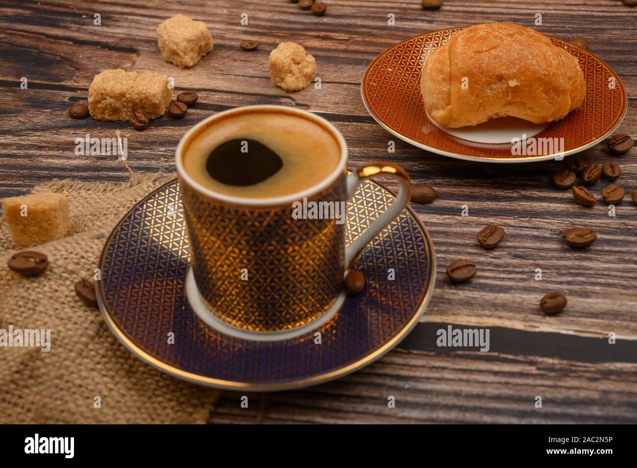 Tazza da caffè, croissant, lo zucchero di canna e i chicchi di caffè su sfondo di legno. Close up Foto Stock