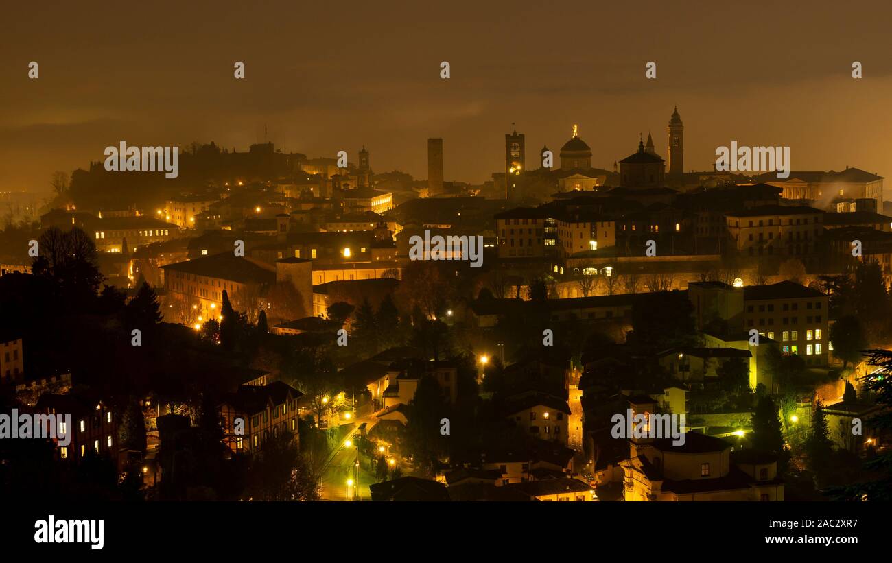 Bergamo, una delle più belle città d'Italia. Un paesaggio fantastico della nebbia sale dalla pianura e copre la città vecchia durante la serata Foto Stock