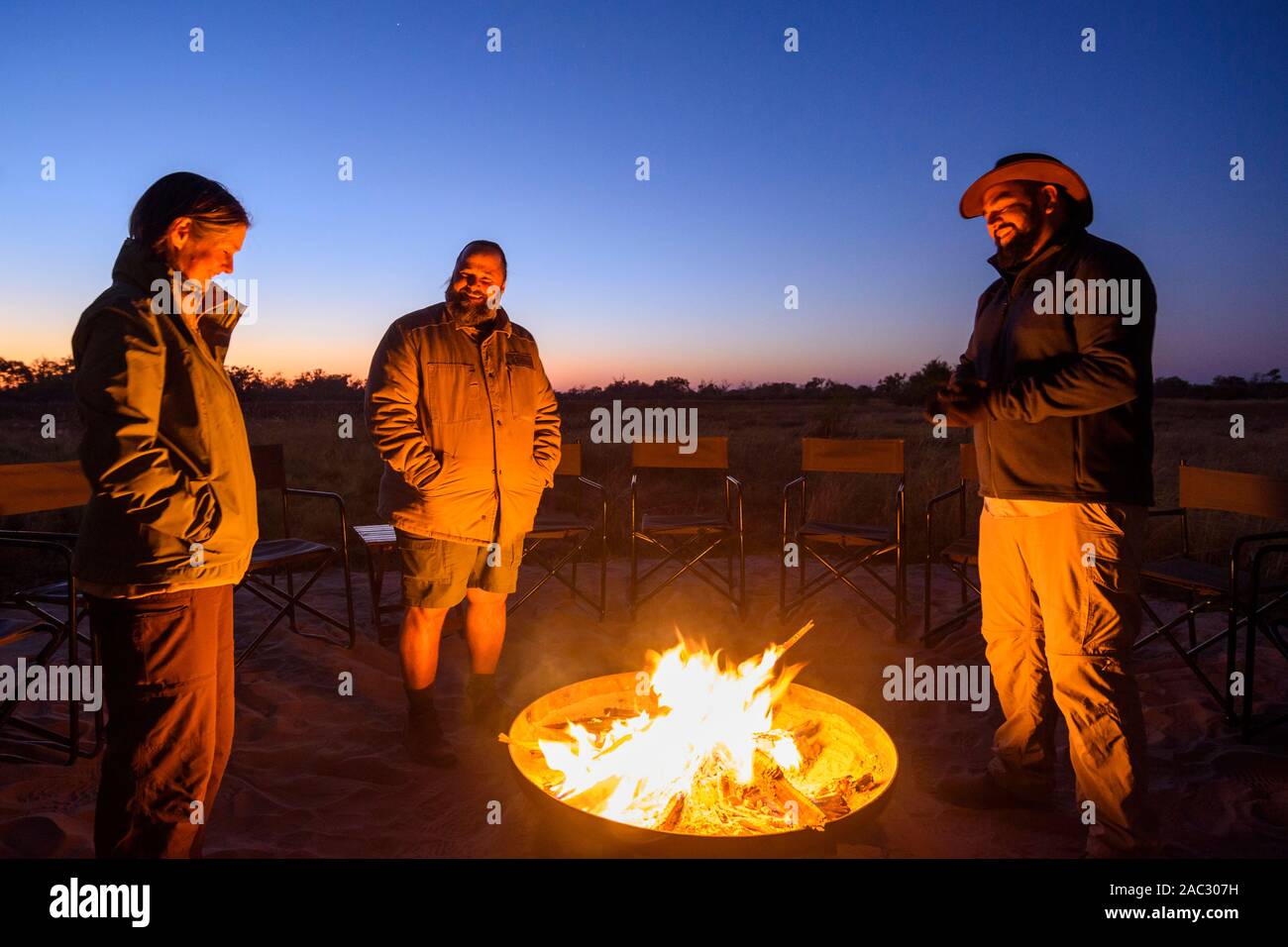 Turisti che si godono il fuoco del campo all'alba, Jackal e Hide campo, Khwai Riserva privata, Delta dell'Okavango, Botswana Foto Stock