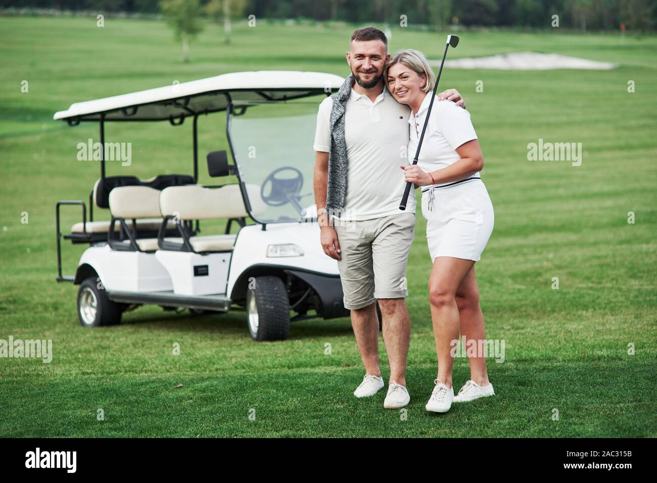 Paio di due golfisti che soggiornano sul prato verde con carrello dietro di loro Foto Stock