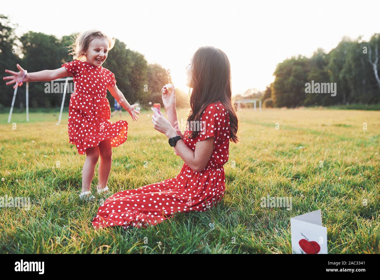 Dare più di me. Ragazza con sua figlia divertendosi con bolle al di fuori seduta sull'erba Foto Stock