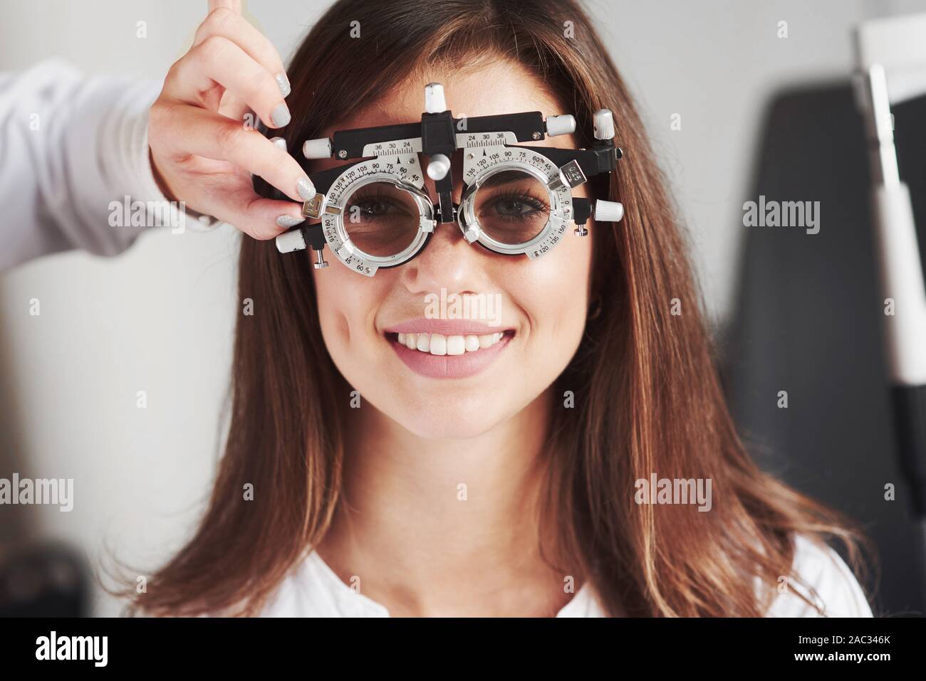 Attraente ragazza sorridente mentre phoropter usura che ottieni tune dal medico Foto Stock