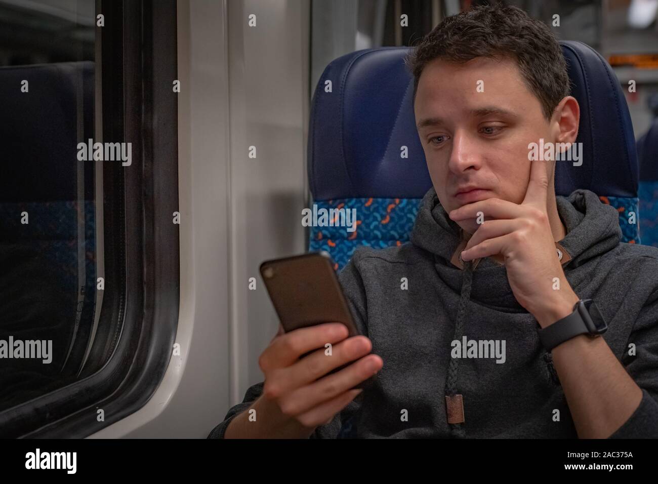Giovane uomo sul treno legge notizie sul suo smartphone Foto Stock