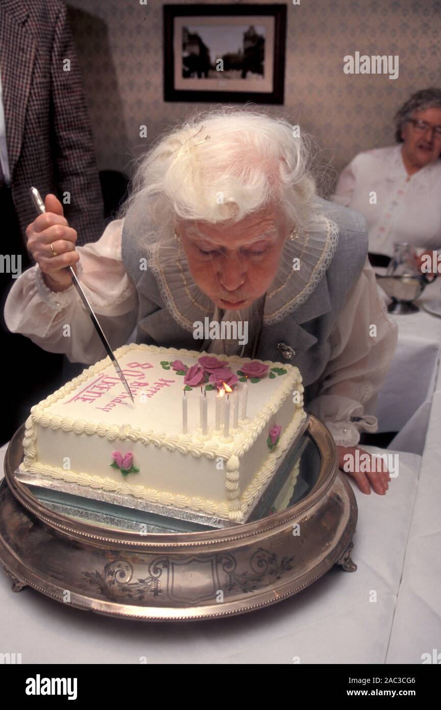 Signora soffiando fuori le candele per il suo ottantesimo compleanno torta Foto Stock