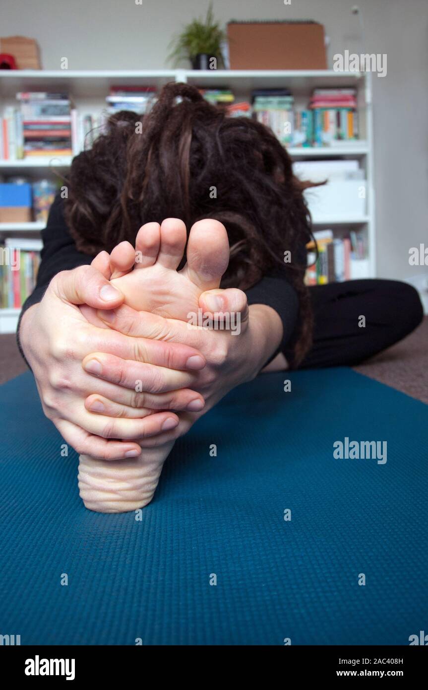 Una donna a praticare yoga nel comfort della propria casa. Testa a ginocchio piegare in avanti / Janu Sirsasana Foto Stock