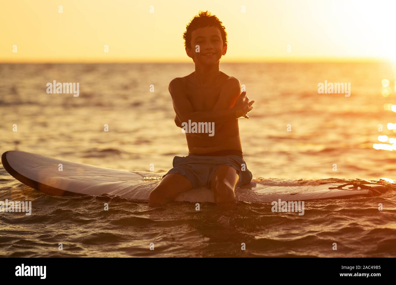 Silhouette di un ragazzo su una tavola da surf in un mare calmo gode del tramonto Foto Stock