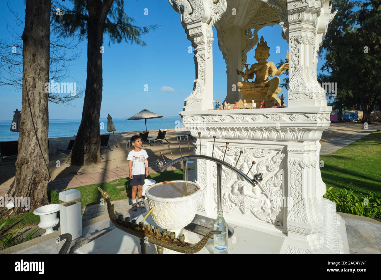 Un giovane ragazzo appare in un santuario con un quattro-di fronte Brahma (dio indù) statua nel parco di Dusit Laguna Hotel, Bang Tao Beach, Phuket, Tailandia Foto Stock