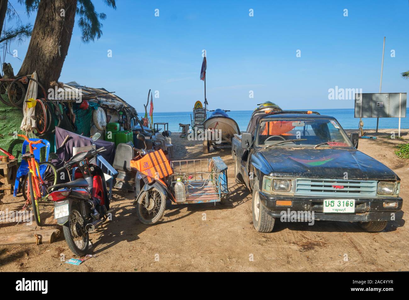 Un unkempt parte di Bang Tao Beach, Phuket, Thailandia, con un battere pick up truck, vecchi motocicli e scartato mobili in spiaggia Foto Stock