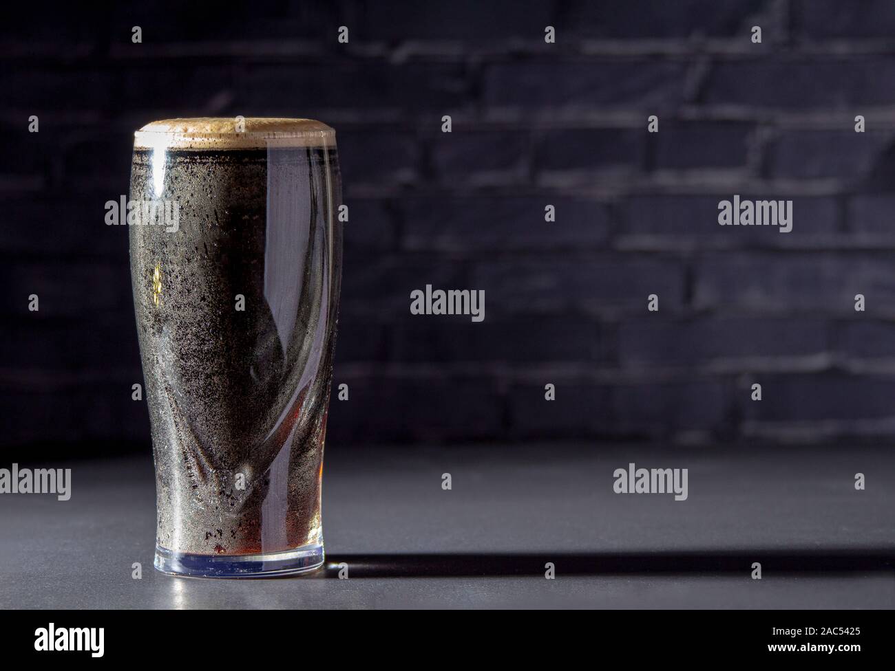 Un buio Irish Stout secca bicchiere di birra con un mattone nero su sfondo Foto Stock