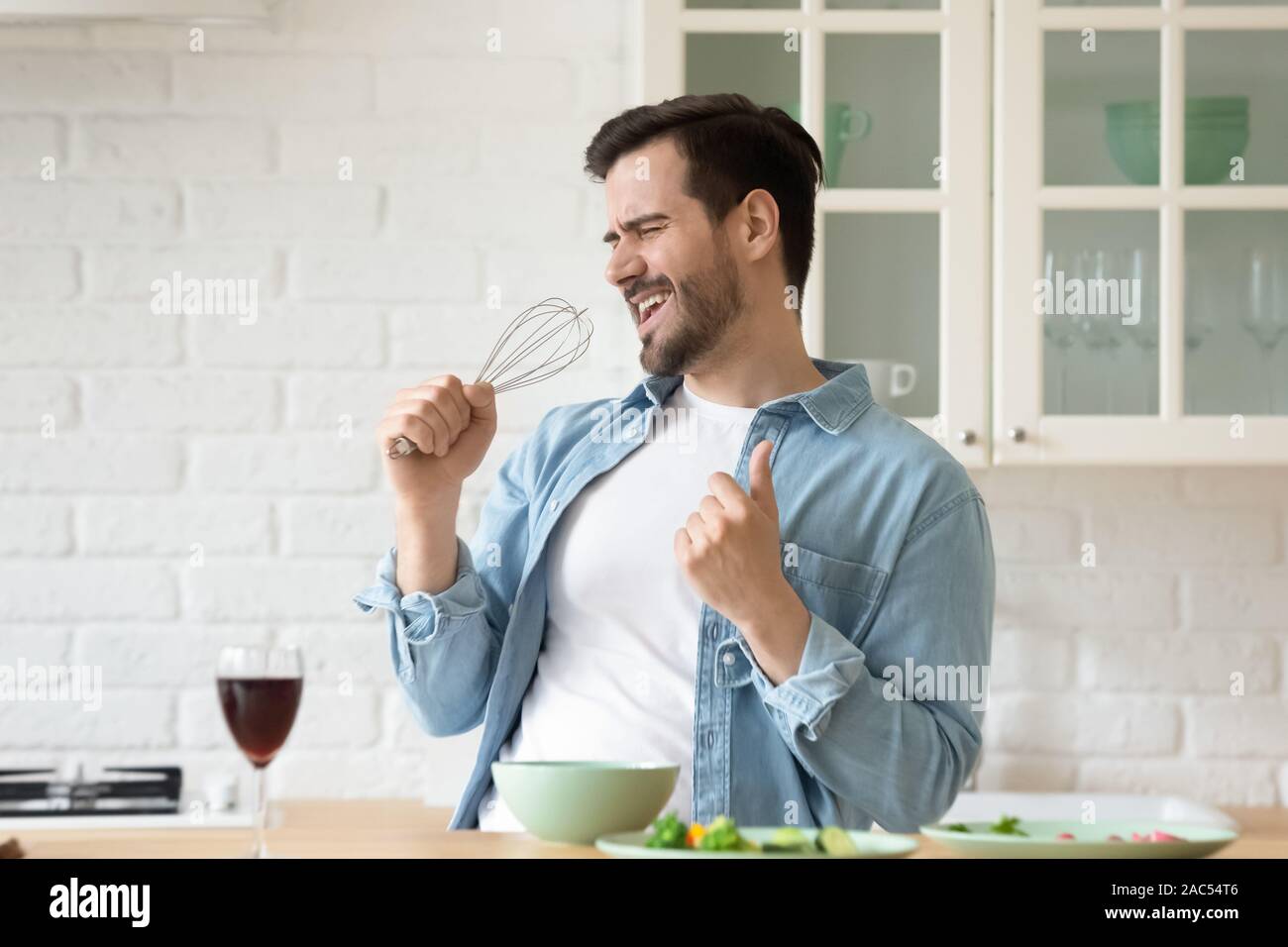 Funny guy cantando tenendo il microfono del lanciapaglia per la cottura nella cucina moderna Foto Stock