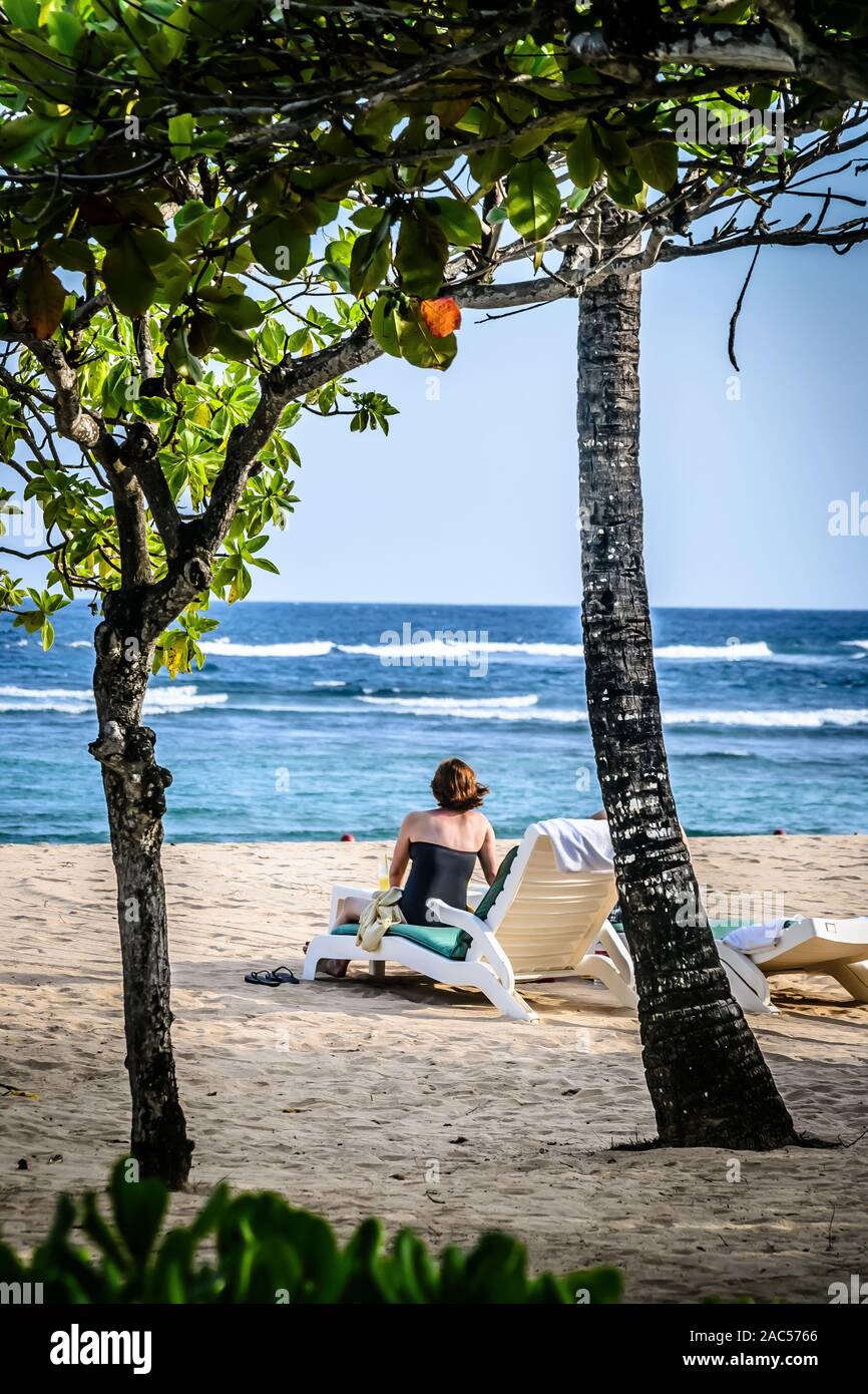 Una donna in costume da bagno seduto su una spiaggia sdraio per prendere il sole sulla spiaggia Foto Stock