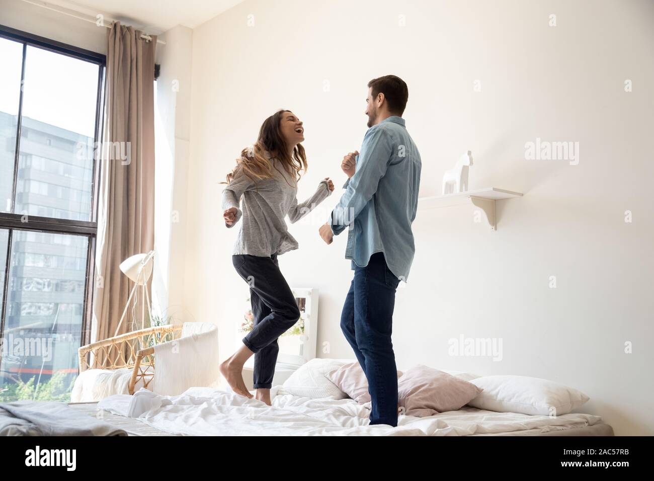 Felice spensierato coppia giovane ridere ballando sul letto insieme Foto Stock