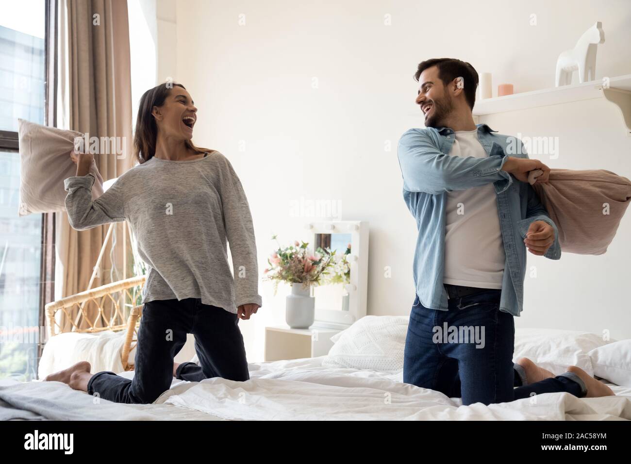 Felice giocoso giovane coppia romantica la riproduzione di lotta di cuscini sul letto Foto Stock