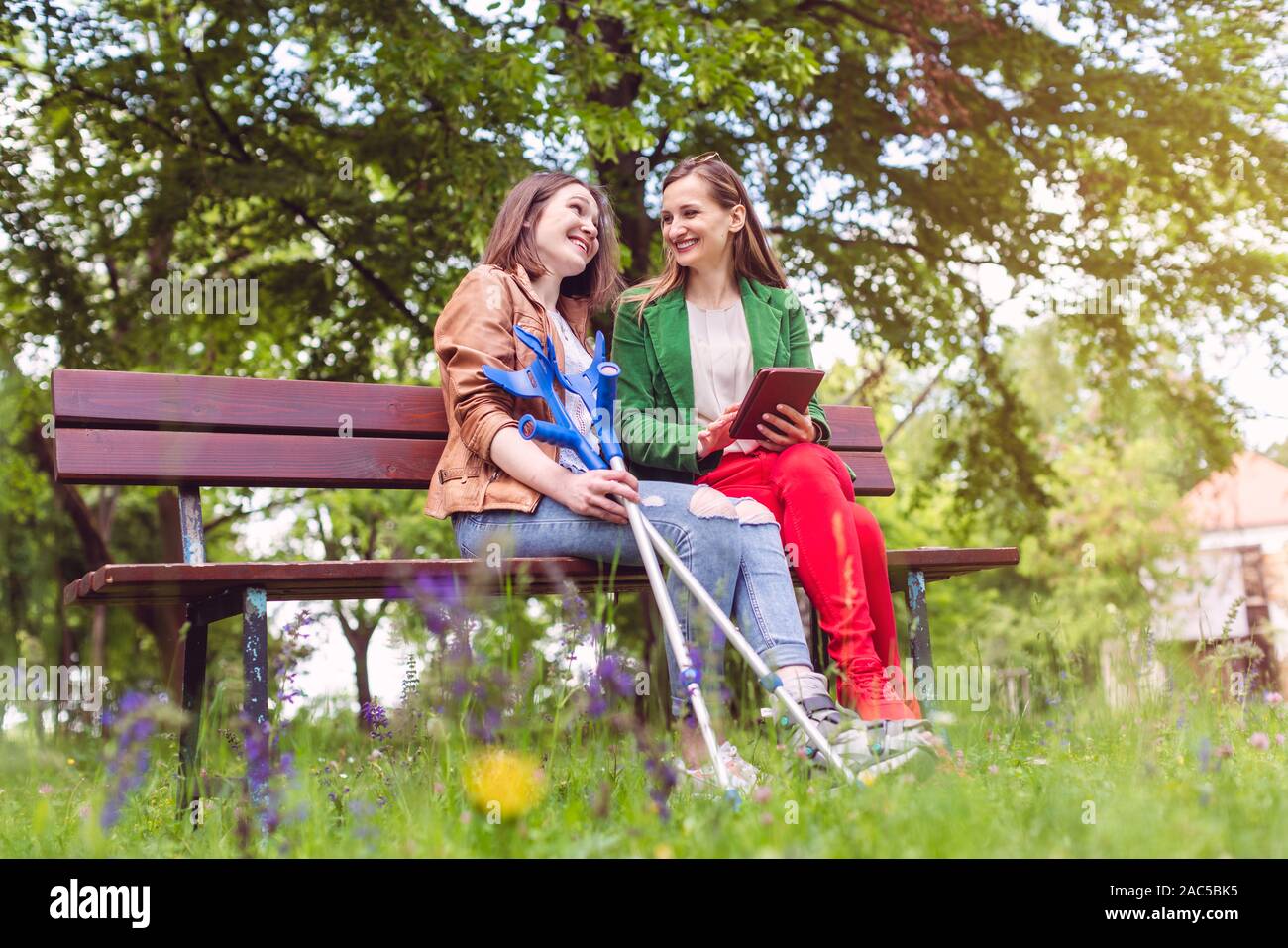 Due amici in un parco, uno con un piede rotto e stampelle Foto Stock