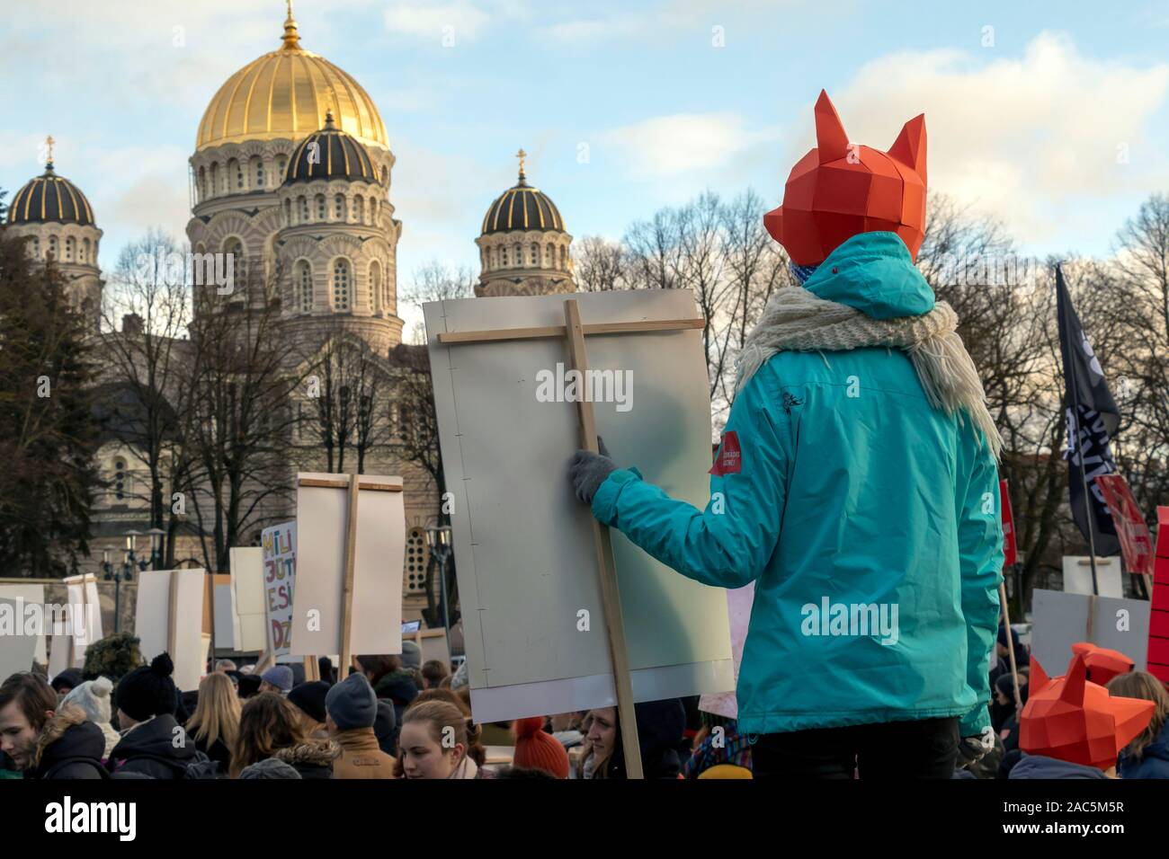 Riga, Lettonia - 30 Novembre 2019 : giovane ragazza in fox maschera poster di tenere in mano e guardare la chiesa piena di speranza di cambiamenti nei diritti degli animali legi Foto Stock