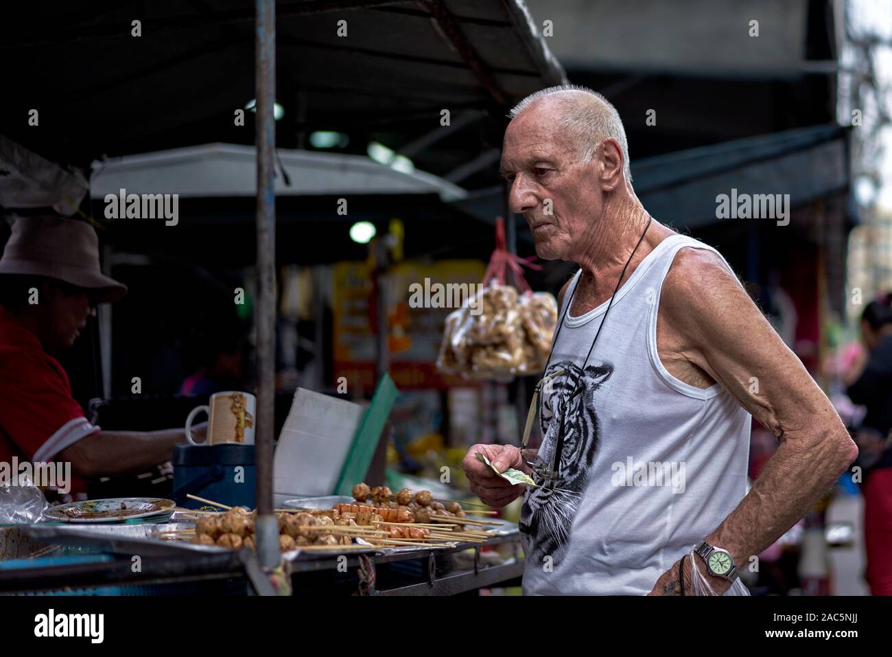 Uomo anziano comprare snack da mangiare in un cibo di strada fornitore. Thailandia del sud-est asiatico Foto Stock