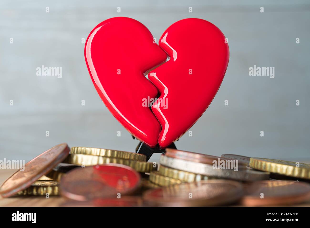 Rosso rotto il giorno di San Valentino cuore su una pila di monete in euro. Amore e Denaro problemi concetto astratto. Sfondo grigio. Foto Stock