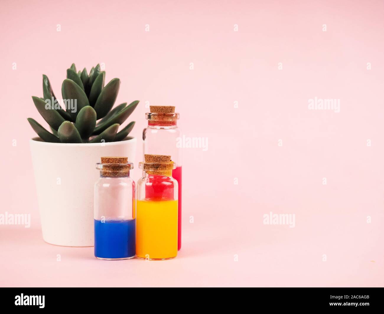 Fiori ed estratti di piante o profumo in piccole bottiglie su sfondo rosa. Tre piccole bolle con liquido rosso blu e giallo, il concetto di Foto Stock
