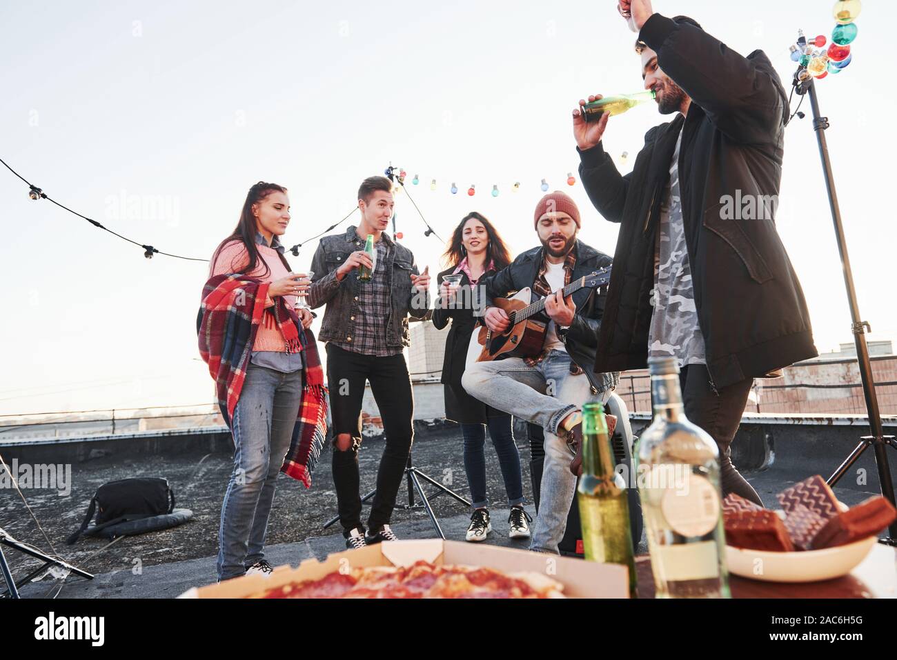 Godendo della canzone. Tabella con il cibo. Weekend sul tetto con chitarra, alcol e pizza Foto Stock