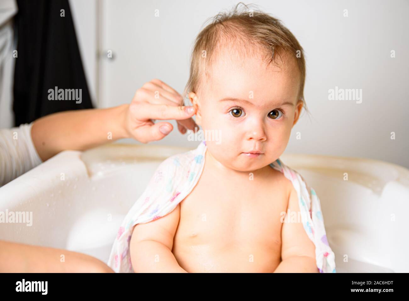 Adorabile bambina prendere un bagno da madre a casa. Pulizia Mom il suo orecchio. Baby il concetto igiene. Foto Stock