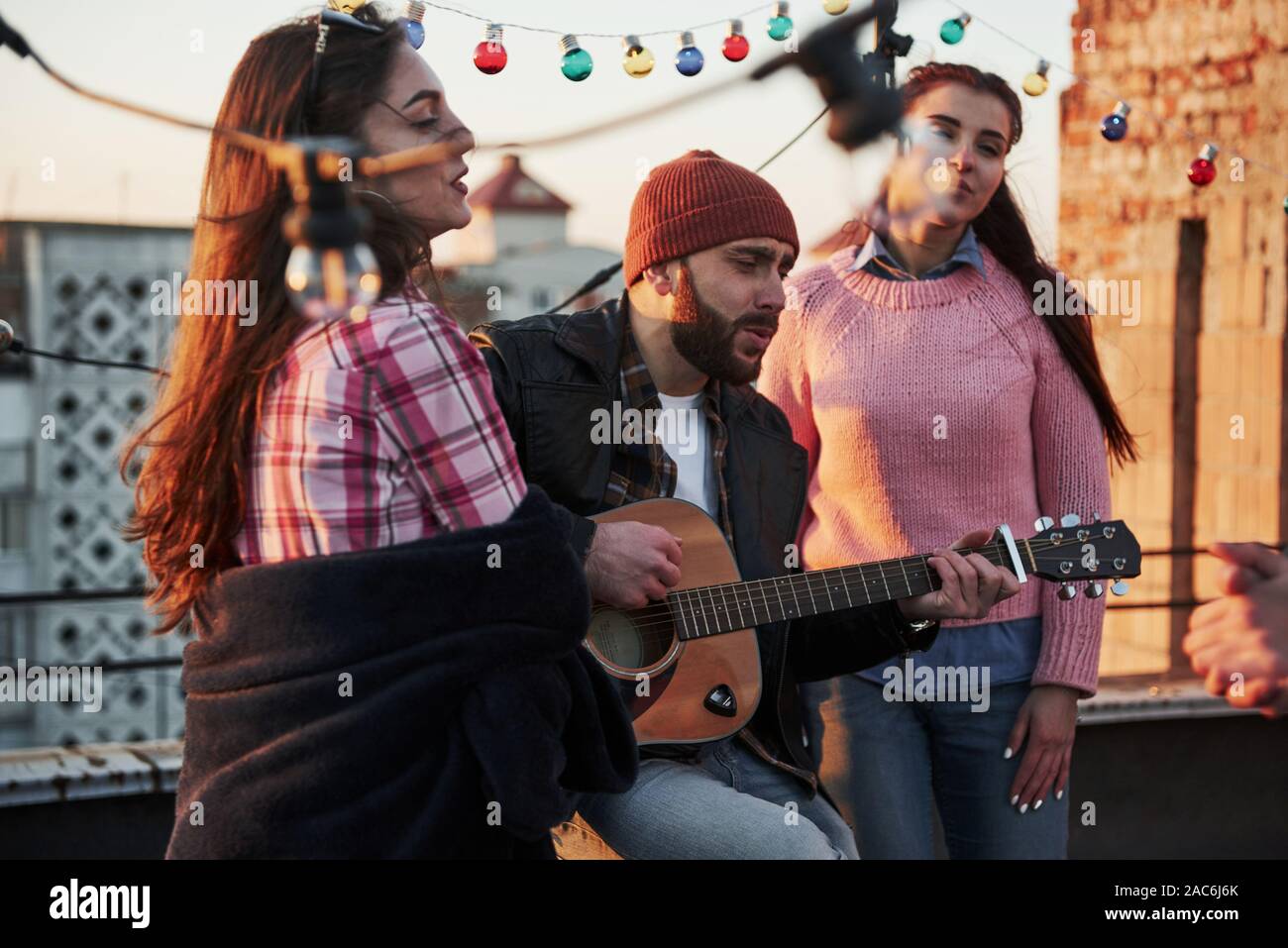 Tre amici godere cantando la chitarra acustica brani sul tetto Foto Stock