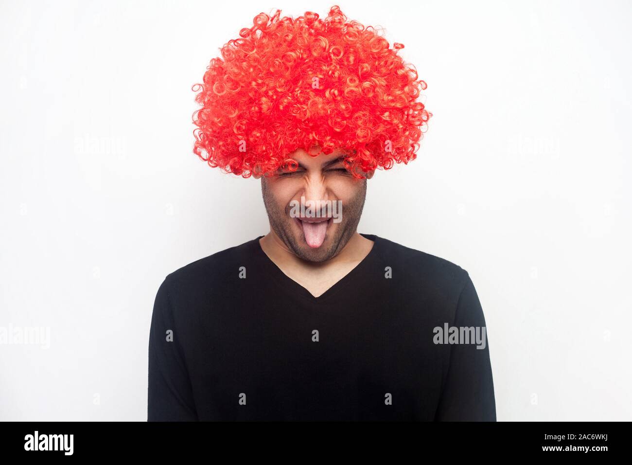 Ritratto di funny crazy strano uomo con setole e ricci parrucca rosso spuntavano lingua, rendendo infantile grimace disobbedienti, eccitante e ingannare aroun Foto Stock