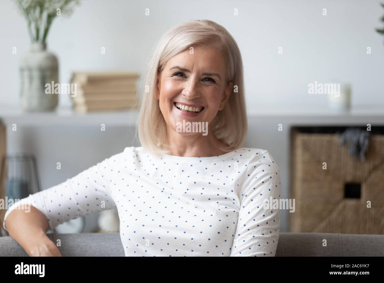 Colpo di Testa di età donna sorridente seduto sul divano guardando in telecamera Foto Stock