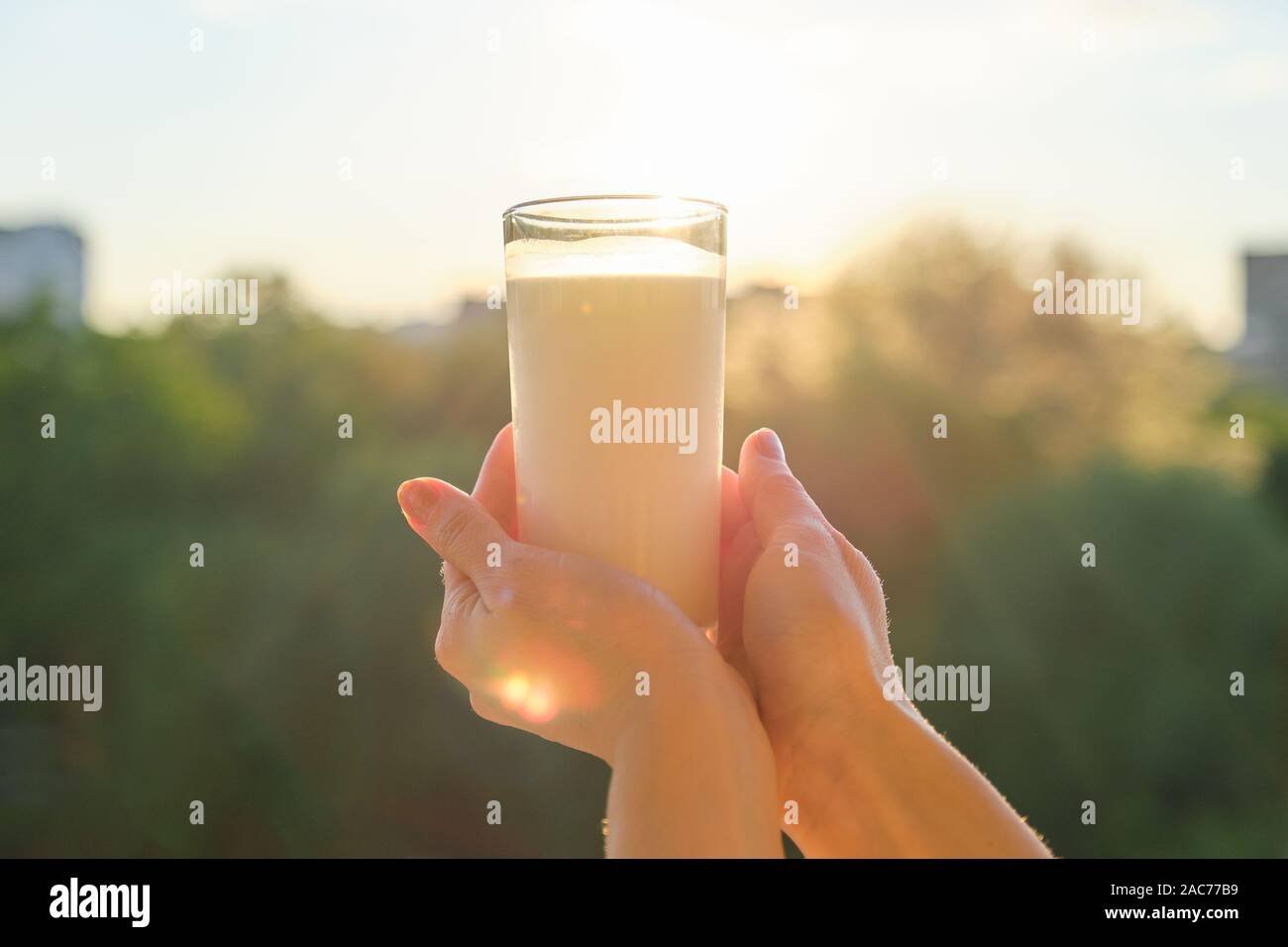 Vetro con latte in mano womans, sfondo tramonto, serale città Foto Stock