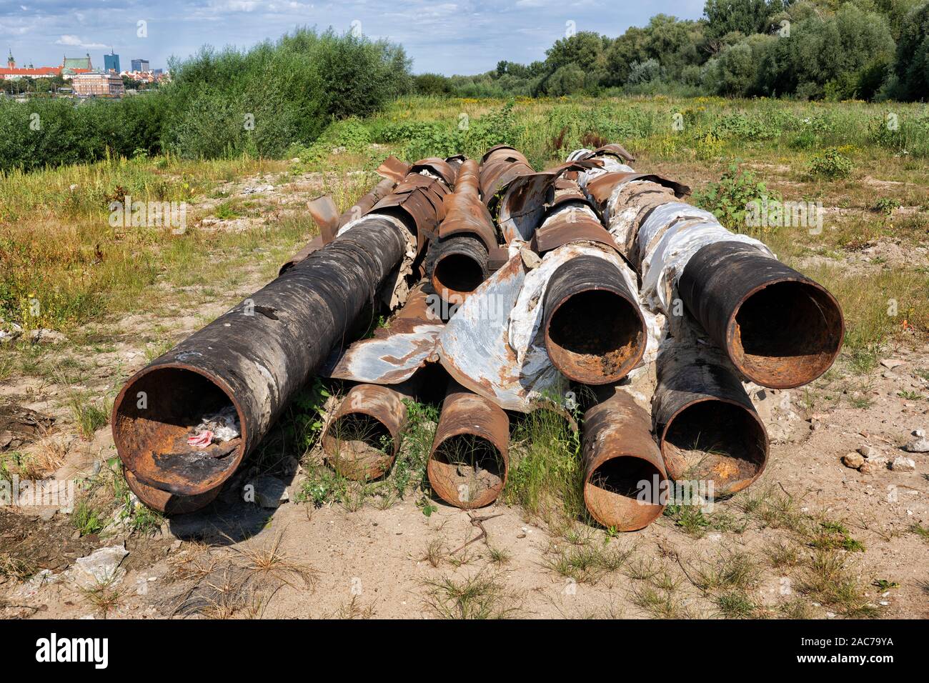 Pila di vecchio metallo arrugginito tubi a sinistra su un campo di argine Foto Stock