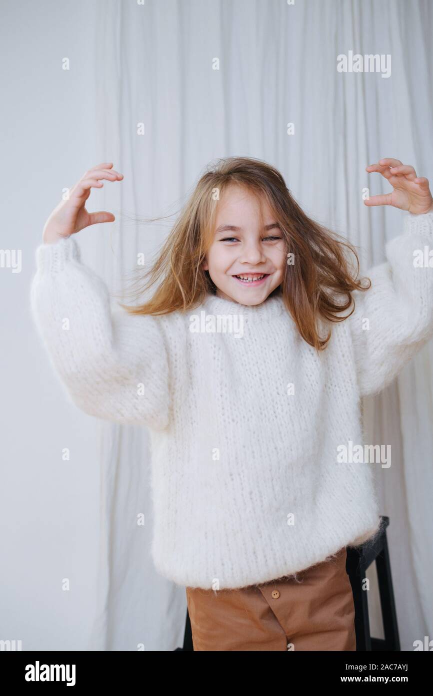 Sorridente bambina con disordinati capelli appena messo su bianco soffice felpa lavorata a maglia. Foto Stock