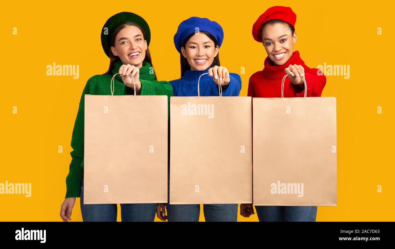 Tre ragazze multietnica Holding Borse shopper su sfondo giallo, Mockup Foto Stock