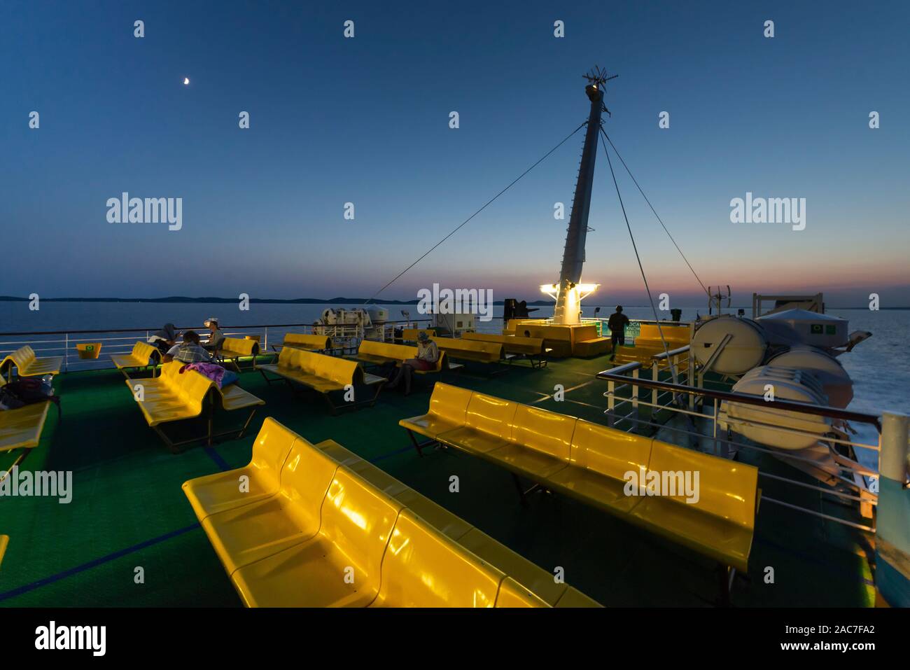 I passeggeri seduti su righe di colore giallo sedili in plastica sul ponte superiore del traghetto nell'arcipelago di Zara dopo il tramonto al tramonto, Croazia Foto Stock