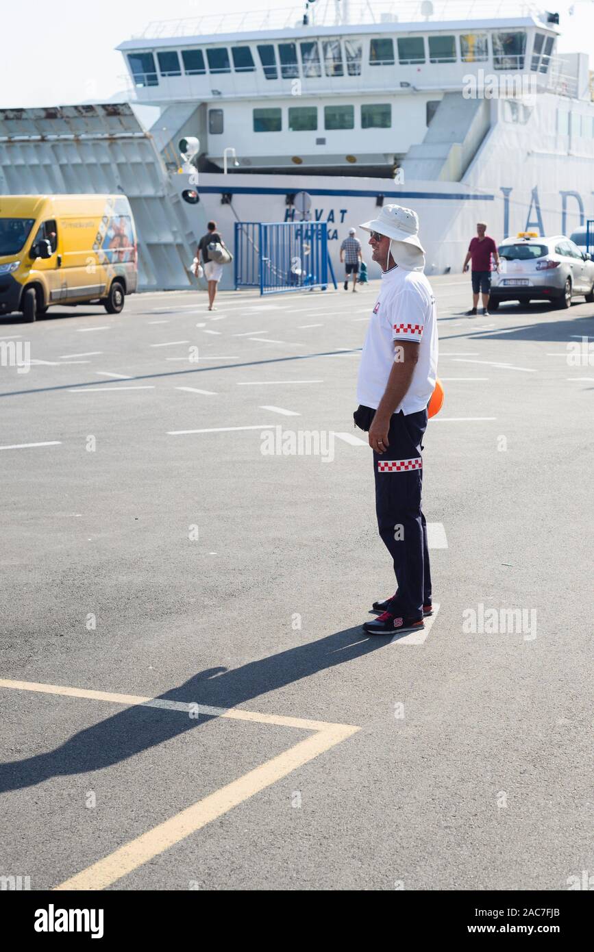 Guida maschio per i veicoli di quando si è a bordo di un traghetto si erge al sole del mattino presso il molo dei traghetti nel porto di Spalato, Croazia Foto Stock