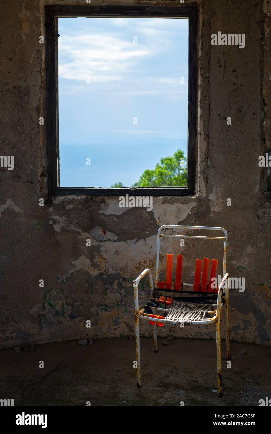 Sedia rotta nella parte anteriore della finestra delle rovine di un palazzo del XIX secolo sulla fortezza il ronzio montagna vicino la città di Velu Luka, isola di Korčula, Croazia Foto Stock