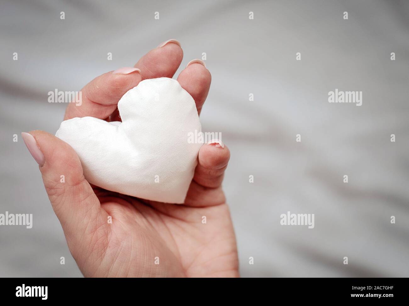 Bianco tessuto artigianale nel cuore della donna di mano su sfondo grigio. Amore, speranza, concetto di donazione. Spazio per il testo. Copia dello spazio. Foto Stock