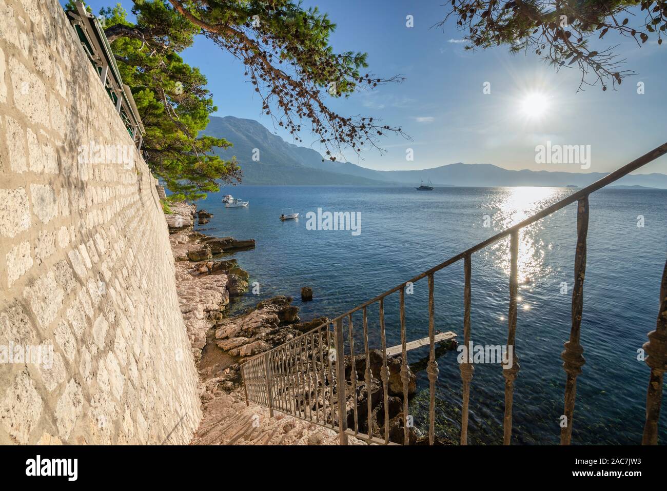 Le scale fino a rocce sull'acqua sotto le mura della città di Korcula con una vista del mare e delle montagne di Peljesac, Dalmazia, Croazia Foto Stock