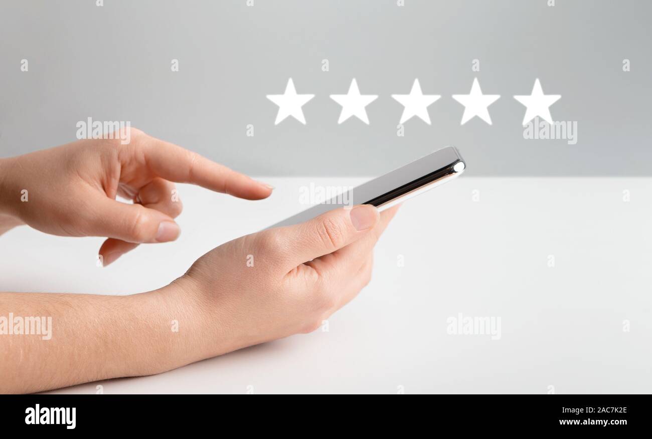 Donna valutazione mobile app sul cellulare su grigio Foto Stock